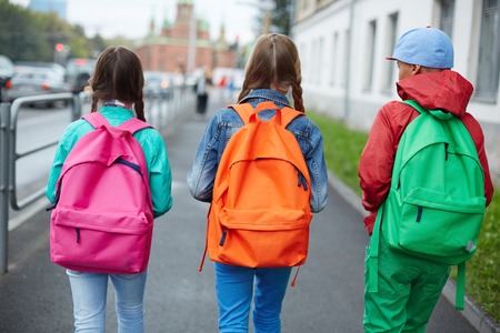 Backs of schoolkids with colorful rucksacks moving in the streetの写真素材