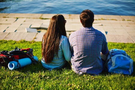 Romantic couple having rest on lawn with river in frontの写真素材