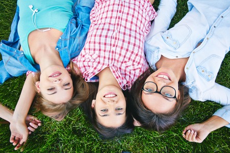 Three cheerful teen girls in casual lying on lawn and looking at cameraの写真素材