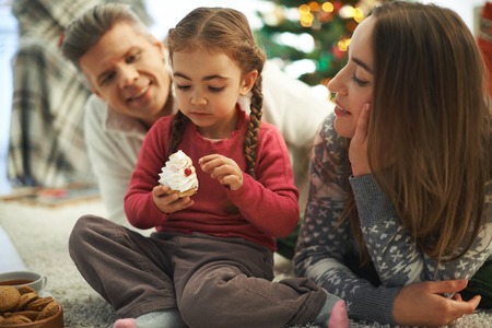 Happy parents looking at their cute daughter with cupcakeの写真素材