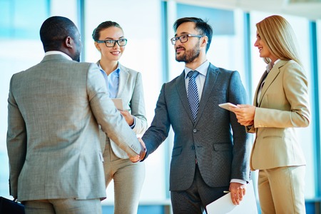 Two businessmen handshaking after signing contract with their female colleagues near byの写真素材