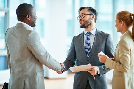 Two businessmen making agreement, their female colleague standing near byの写真素材