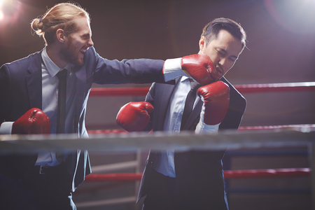 Powerful businessman in suit and boxing gloves attacking his rivalの写真素材