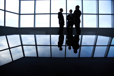 Three business partners having a discussion standing against a panoramic window in officeの写真素材