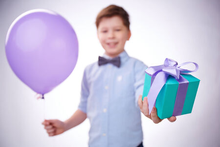 Little boy holding giftbox in one hand and lilac balloon in the otherの写真素材