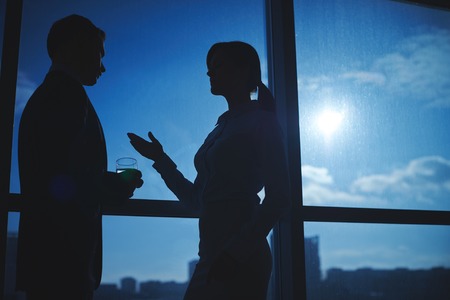 Outlines of businessman and businesswoman communicating by the windowの写真素材