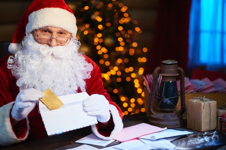 Happy Santa Claus looking at camera while putting discount card into envelopeの写真素材