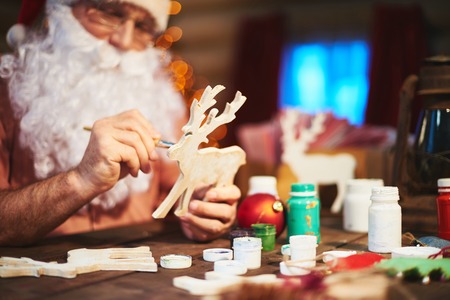 Senior Santa man painting wooden deer with gouacheの写真素材