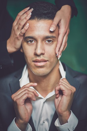 Handsome guy in formalwear with female hands on his head looking at cameraの写真素材