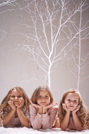 Three calm girls looking at camera while lying in winter forestの写真素材