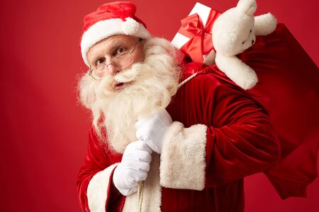 Portrait of Santa carrying huge red sack with xmas gifts for kidsの写真素材