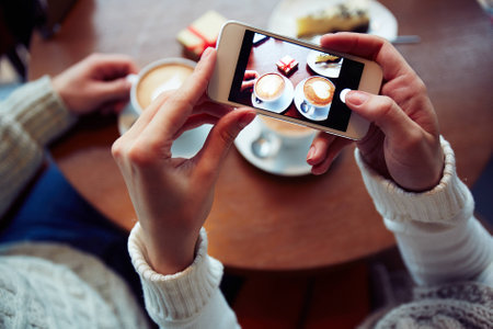 Two cups of cappuccino, cheesecake and small giftbox on cellphone displayの写真素材