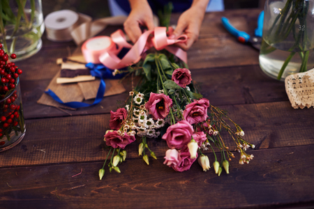 Hands of decorator tying bunch of flowers up with pink ribbonの写真素材