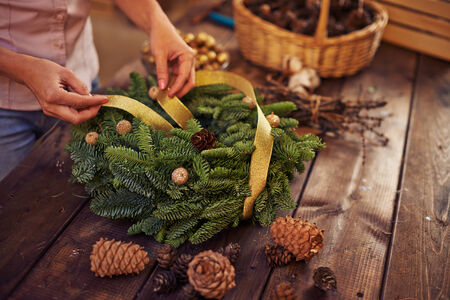 Female hands with golden ribbon decorating coniferous wreathの写真素材