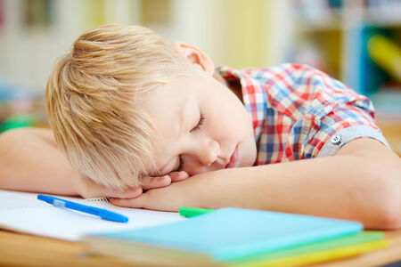 Tired elementary pupil napping by desk after lessonsの写真素材