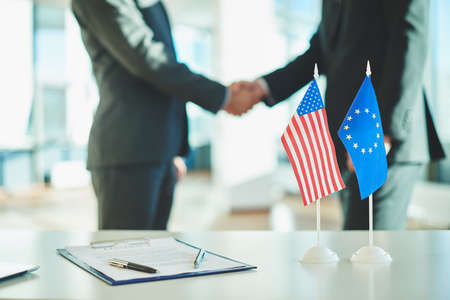 American flag, flag of European Union and contract on background of businessmen handshakingの写真素材