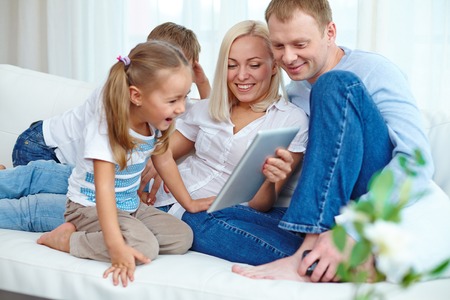 Happy parents and their two children resting on sofa with touchpad