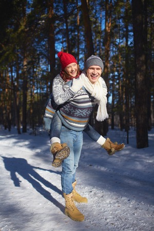 Joyful couple in knitted winterwear having fun in winter forestの写真素材
