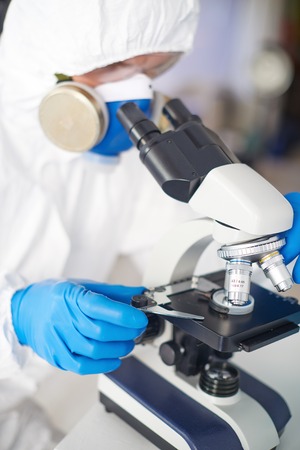 Male scientist in protective clothing looking in microscope