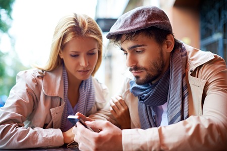 Young couple using cellphone in cafeの写真素材