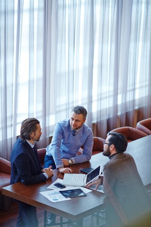 Group of male managers gathered by table in officeの写真素材