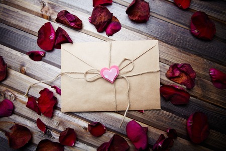 Letter of love sealed by small decorative heart on its top and rose petals near by