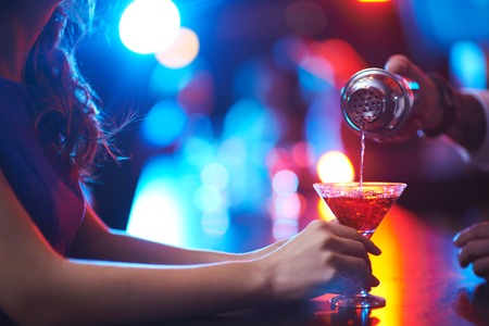 Young woman holding martini glass while barman pouring cocktailの写真素材