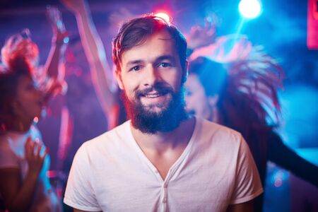 Bearded guy looking at camera while ecstatic friends dancing on backgroundの写真素材