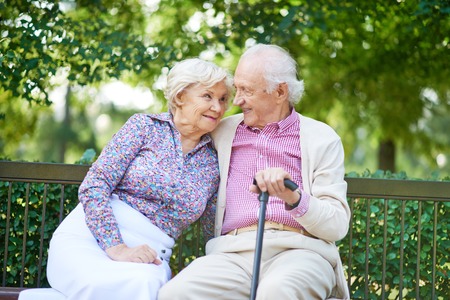 Happy senior couple sitting on bench in the park and talkingの写真素材