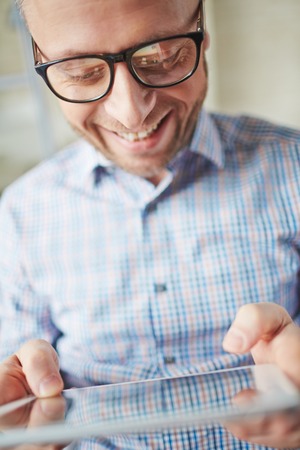 Smiling businessman in eyeglasses browsing in touchpadの写真素材