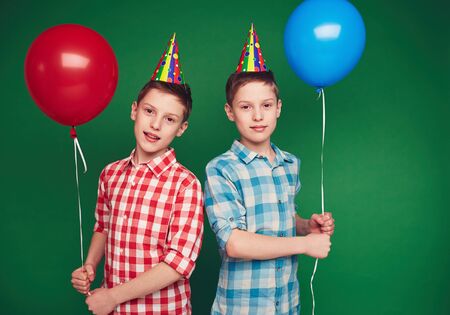 Cute twins with balloons looking at cameraの写真素材