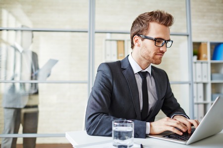 Young businessman in formalwear typing on laptopの写真素材