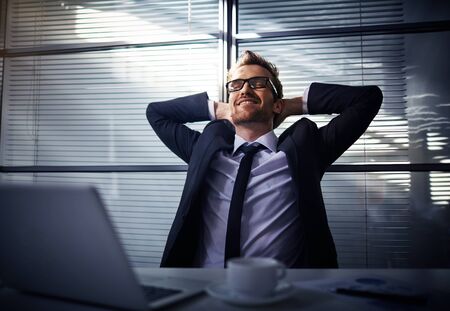 Happy young businessman dreaming in officeの写真素材