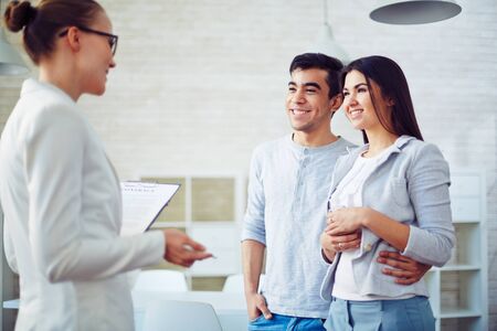 Young couple listening to female agent in realtor officeの写真素材