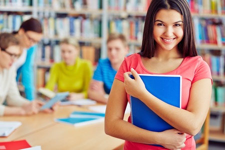 Cheerful student with copybook looking at camera in libraryの写真素材
