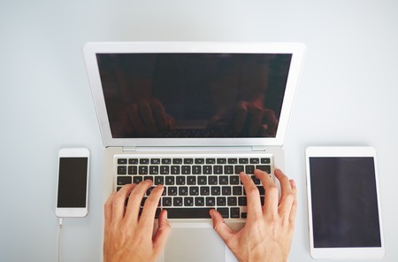 Human hands typing on laptop keypad between smartphone and digital tabletの写真素材