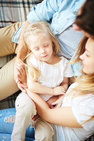Cute little girl sleeping on her parents kneesの写真素材