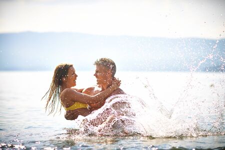 Young man holding his happy wife while both splashing waterの写真素材