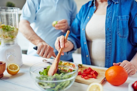 Senior female mixing salad ingredients in glass bowlの写真素材