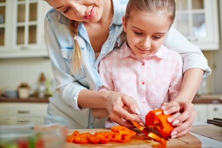 Little girl cutting fresh pepper with help of her motherの写真素材