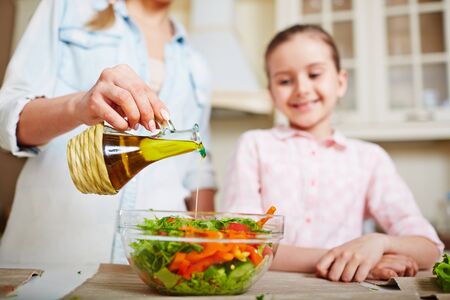 Young woman dripping olive oil into bowl with fresh vegetable saladの写真素材
