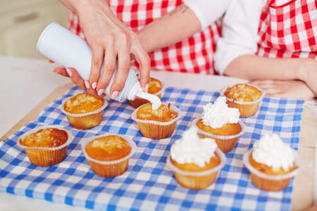 Hands of young woman with cream decorating baked muffinsの写真素材