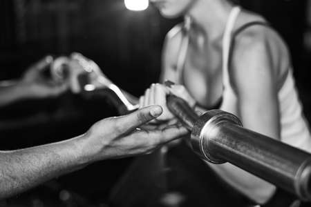 Hand of trainer helping girl lift metal weightの写真素材