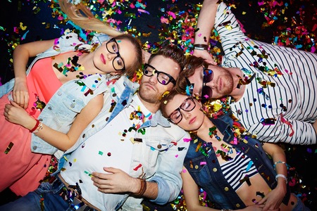 Young friends sleeping in confetti on the floor in nightclub after party