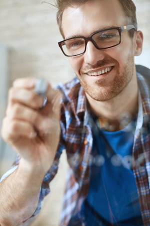 Smiling businessman in eyeglasses making notes on transparent boardの写真素材