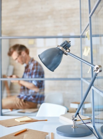Workplace with lamp, papers and pencils with sitting businessman on backgroundの写真素材