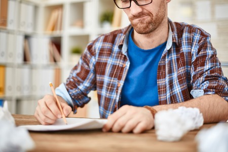 Young businessman with pencil writing down his ideas with crumpled sheets near byの写真素材