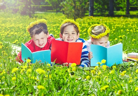 Cute children in dandelion wreaths reading on lawnの写真素材