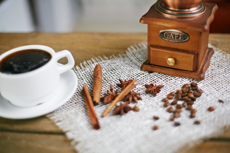 Wooden coffee grinder, coffee beans, star anise, cinnamon sticks and cup of black coffeeの写真素材