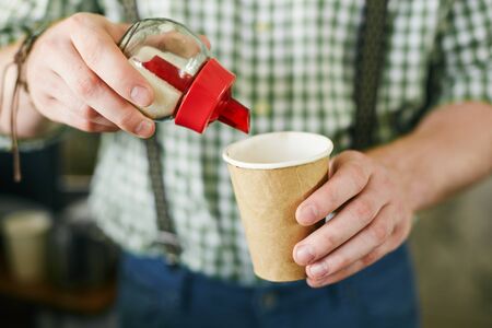 Hands of barista adding sugar in takeout paper cup with coffeeの写真素材